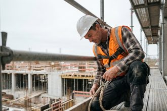 Ouvrier sur échafaudage inspectant une corde de sécurité dynamique avec harnais intégral sur chantier en hauteur
